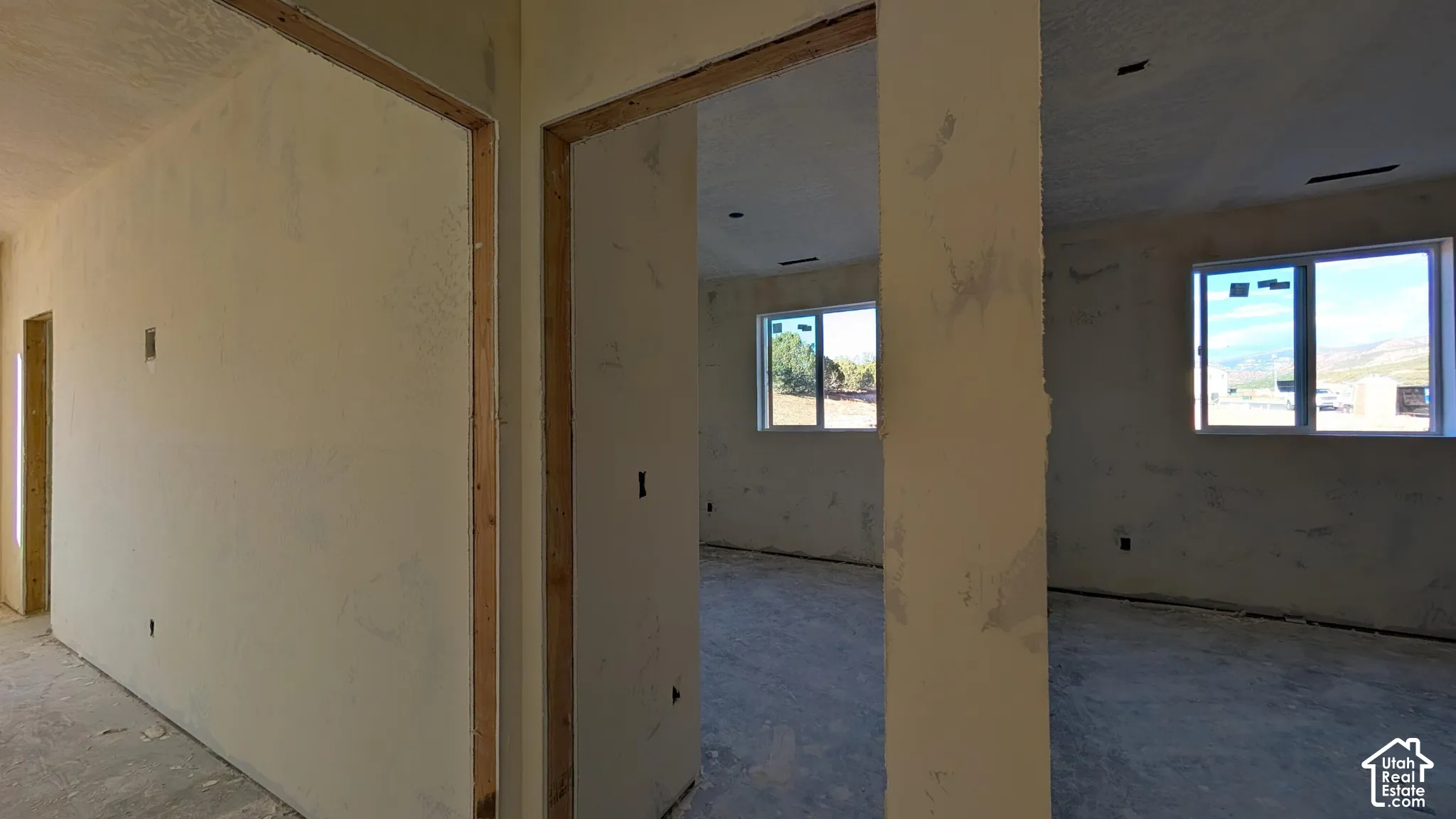 Interior space featuring unfinished drywall, white-frame sliding windows, and exposed doorway framing