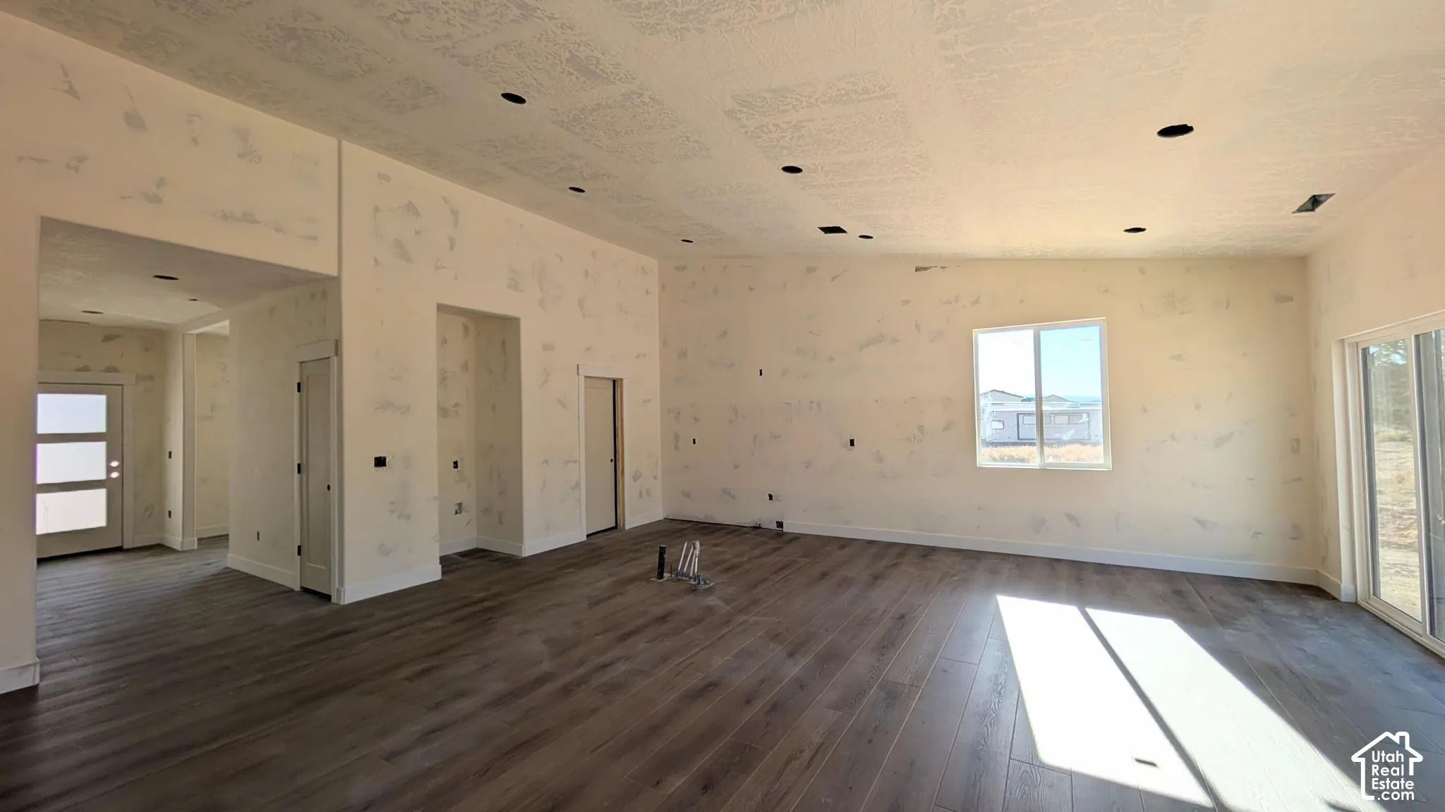Open-concept interior featuring vaulted ceilings, recessed lighting, wood-finish flooring, sliding glass door, and multi-panel entry door