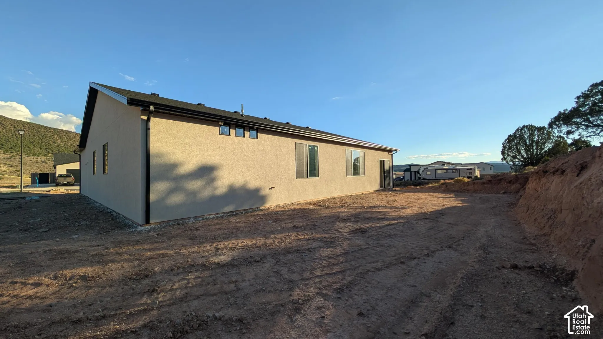 Stucco exterior featuring dark-trimmed rooflines, multi-pane windows, and high-set transom windows, situated against a backdrop of mountainous terrain