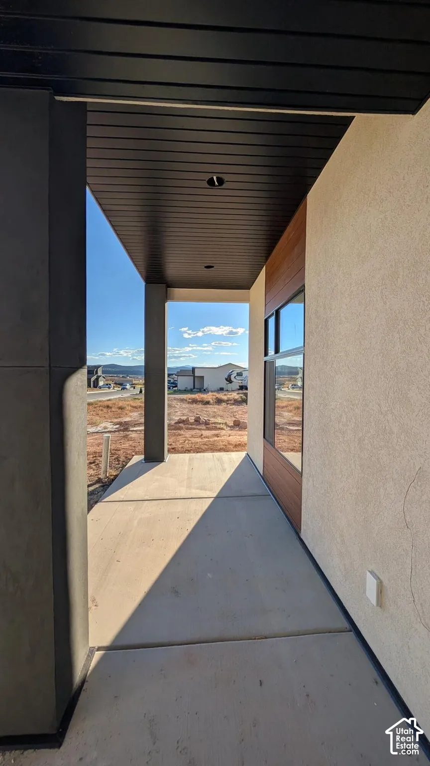 Covered entryway featuring a stained wood-panel ceiling, concrete flooring, recessed lighting, and mixed-material facade consisting of smooth stucco and natural wood cladding