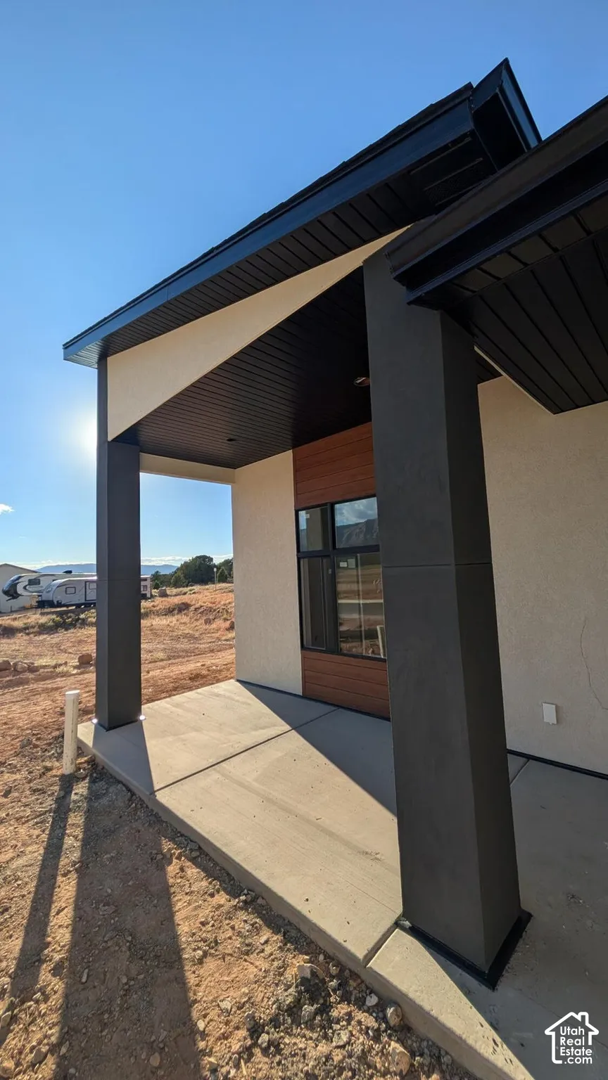 Modern covered patio featuring a concrete slab, high-contrast dark structural columns, a wood-finished accent wall, and black window framing
