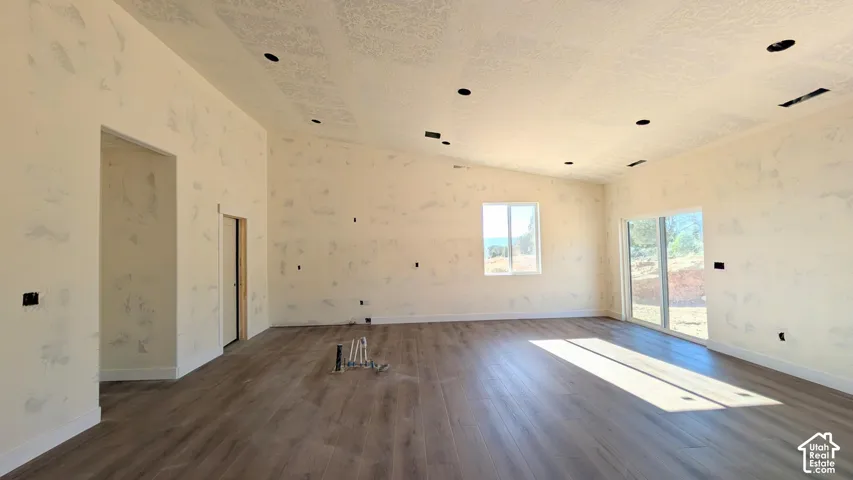 Open-concept interior featuring vaulted ceilings, wood-finish flooring, recessed lighting, and large windows providing natural light