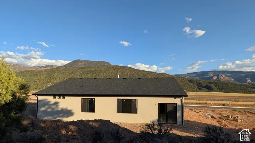 Stucco exterior featuring dark-trimmed windows, a shingled gable roof, and mountain terrain backdrop
