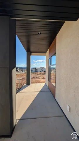 Covered entryway featuring a stained wood-panel ceiling, concrete flooring, recessed lighting, and mixed-material facade consisting of smooth stucco and natural wood cladding