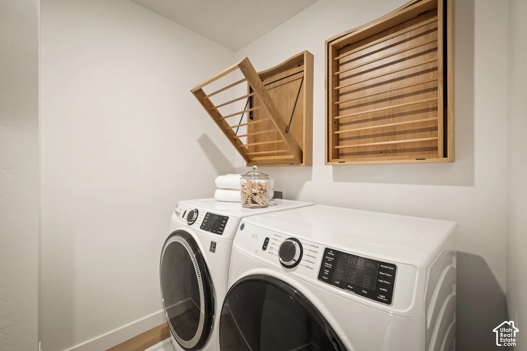 Wall-mounted wood-finish drying racks featuring retractable frames, accompanied by white front-loading laundry appliances