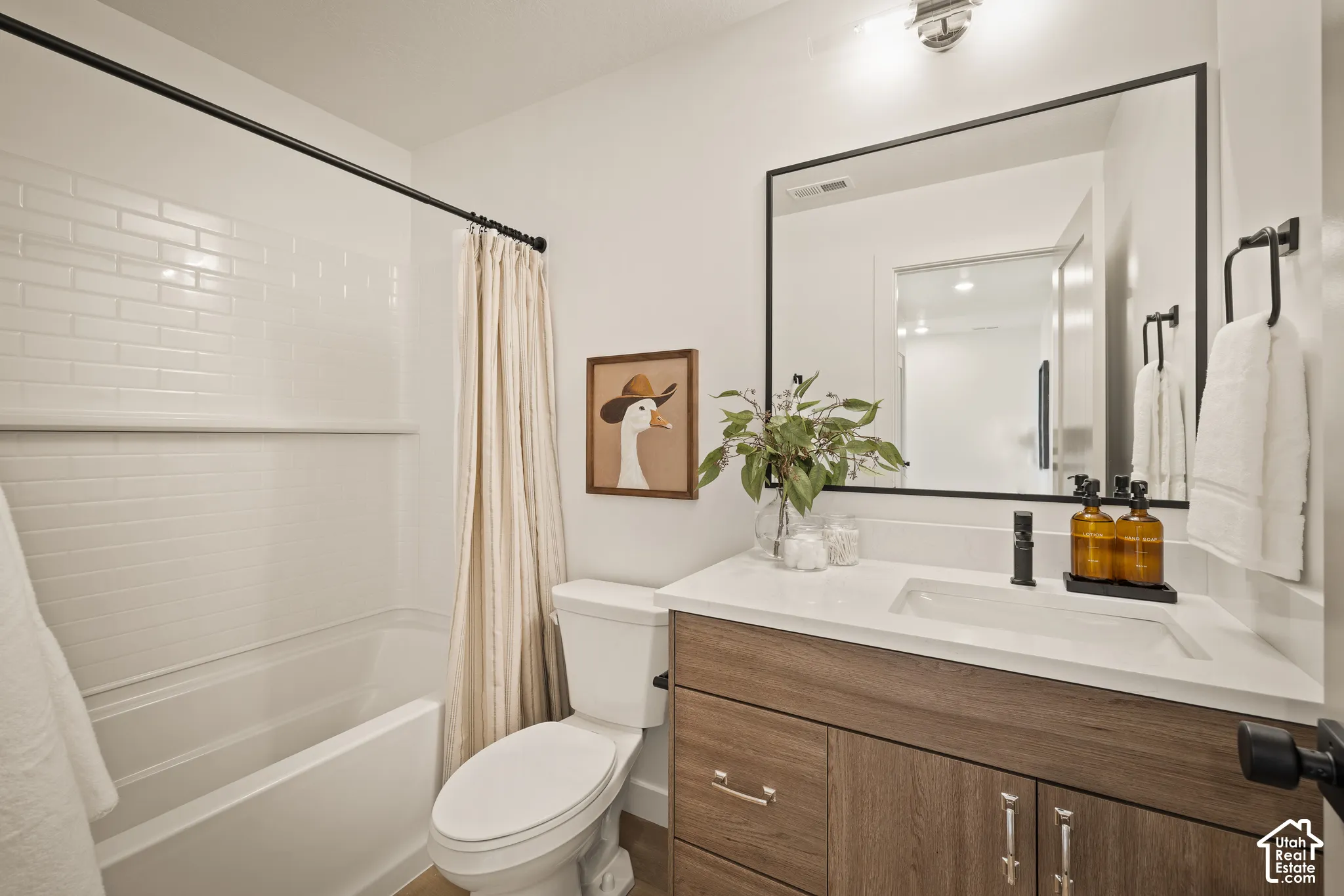 Bathroom featuring a wood-finish vanity with a stone-composite countertop, integrated sink, matte black hardware, and a tub-shower combination with white subway tile surround