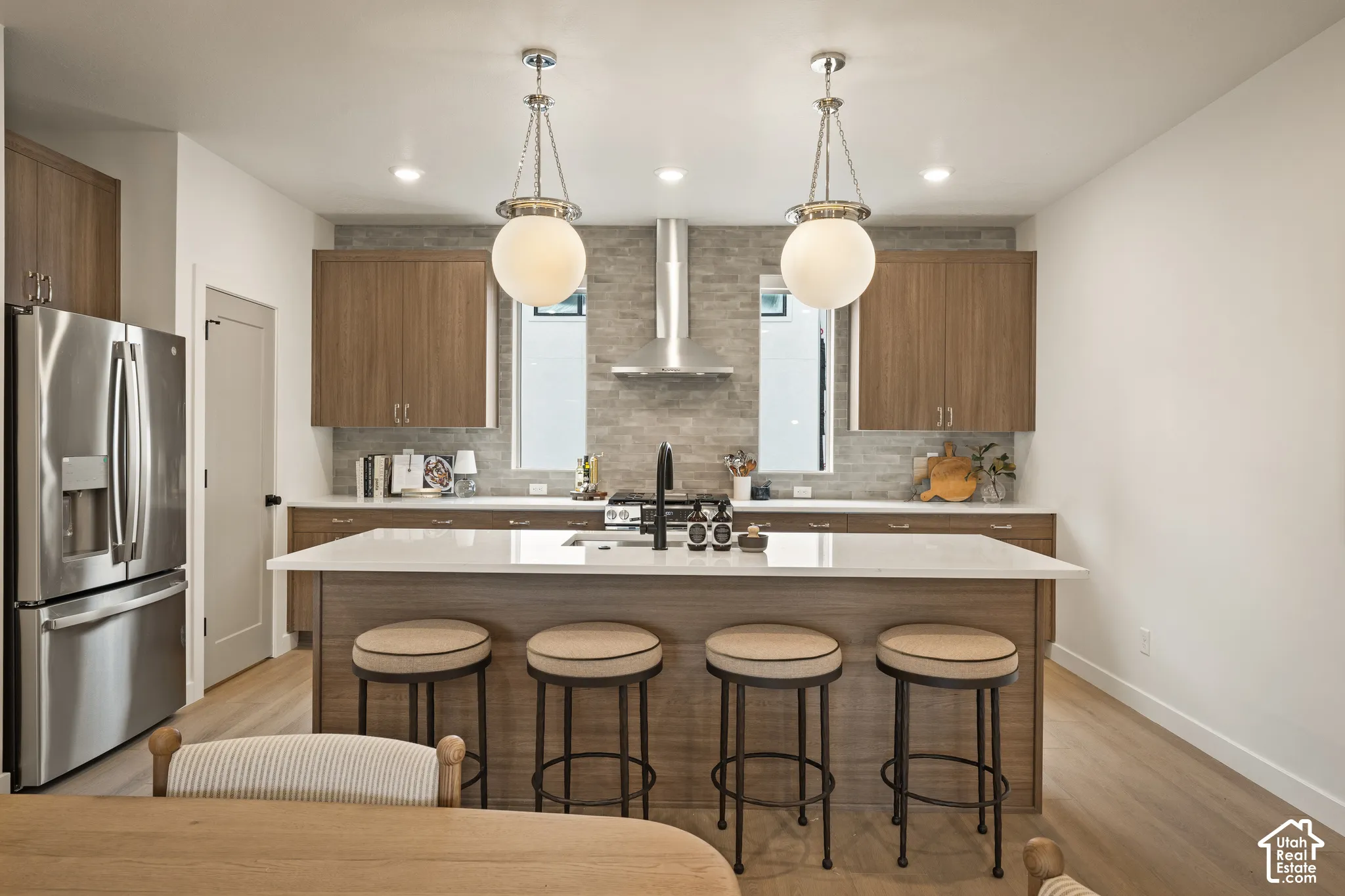 Kitchen featuring a central island with a solid-surface countertop, stacked-stone backsplash, stainless steel appliances, flat-panel wood-finish cabinetry, and globe-style pendant lighting