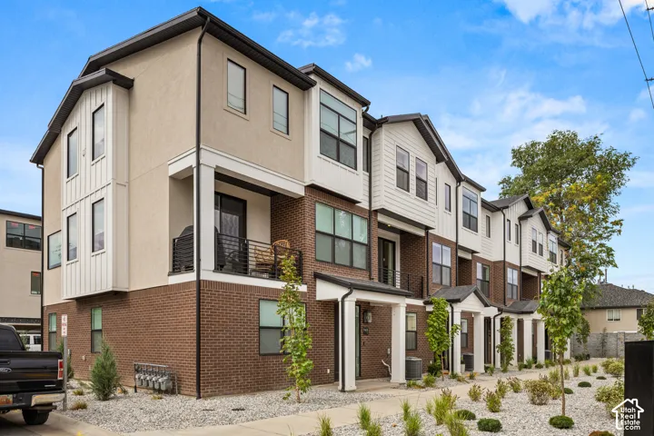 Multi-level townhome exterior featuring brick masonry, vertical siding, private balconies with metal railings, and xeriscaped landscaping