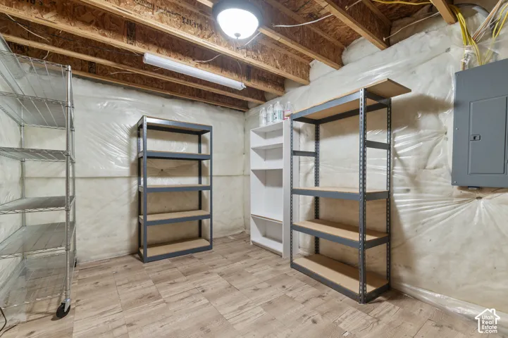 Storage area featuring wood-finish tile flooring, exposed timber ceiling joists, vapor barrier wall insulation, and a wall-mounted electrical panel
