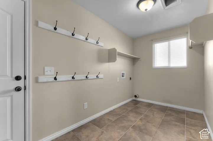 Utility room featuring stone-tile flooring, dual rows of mounted wall hooks, integrated shelving, and a window with blinds