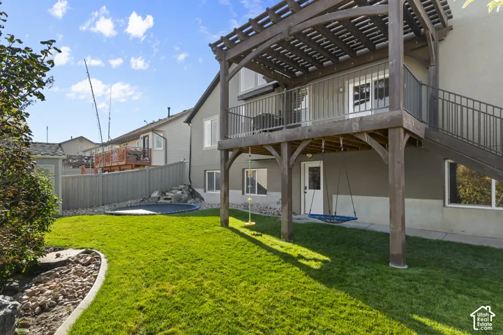 Backyard featuring a wood-framed pergola, elevated deck with iron railings, landscaped lawn, stone rock edging, and perimeter fencing