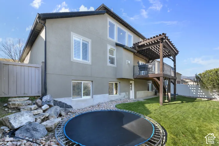 Stucco exterior featuring a raised wooden pergola, metal balcony railing, landscaped stone rockery, and fenced yard