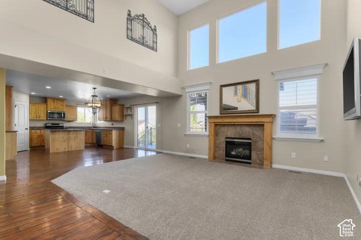 Double-height ceiling, gas fireplace with tile surround and wood mantel, wood-finish flooring, multi-pane windows, and kitchen cabinetry with integrated appliances