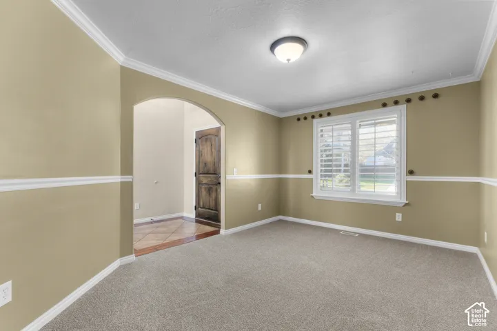 Room featuring crown molding, chair rail trim, arched entryway, and interior shutters
