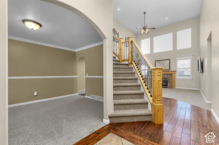 Entryway featuring high ceilings, wood-finish flooring, staircase with natural wood railings and metal balusters, and a fireplace with a stone-surround mantel
