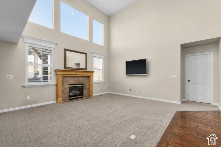 High-ceilinged room featuring expansive multi-tier windows, a fireplace with a stone-surround and wood-finish mantel, and wood-finish flooring