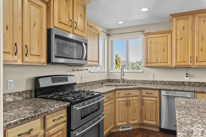 Kitchen featuring knotty wood cabinetry, stone-patterned countertops, stainless steel appliances, and a dual-basin corner sink with a pull-down faucet