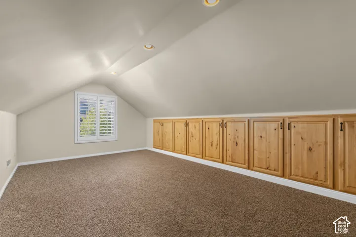 Vaulted ceilings featuring recessed lighting, built-in light-tone wood cabinetry, and a window with plantation shutters