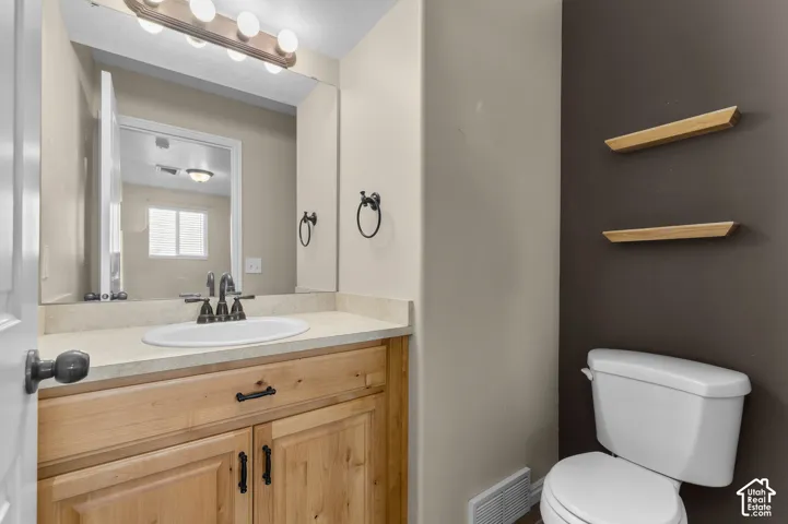 Bathroom featuring a wood vanity, solid-surface countertop with an integrated basin, matte black fixtures, and dual wall-mounted floating wood shelves