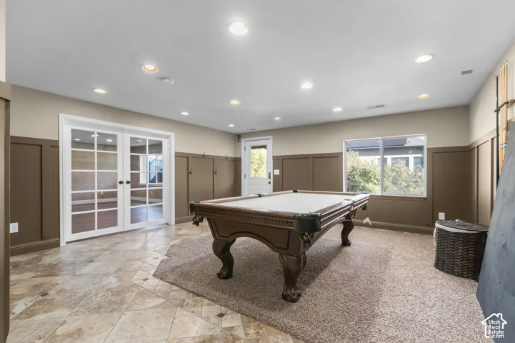 Room featuring tile flooring, wall-mounted wainscoting, recessed lighting, glass-paneled double doors, and a window with natural exterior exposure