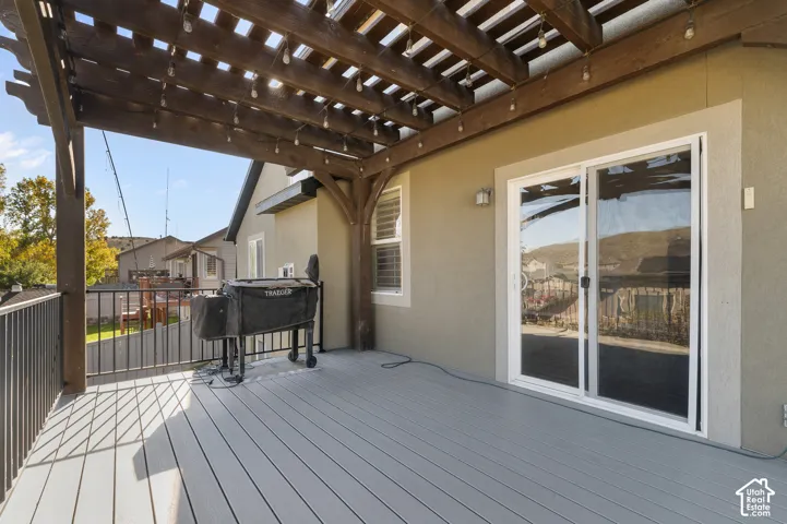 Covered outdoor deck featuring a dark wood-finish pergola, grey composite decking, metal railing, and a sliding glass door