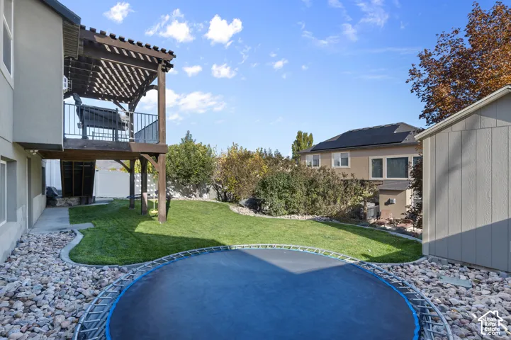Backyard featuring a raised wooden pergola, manicured lawn, river rock landscaping, and a detached storage shed