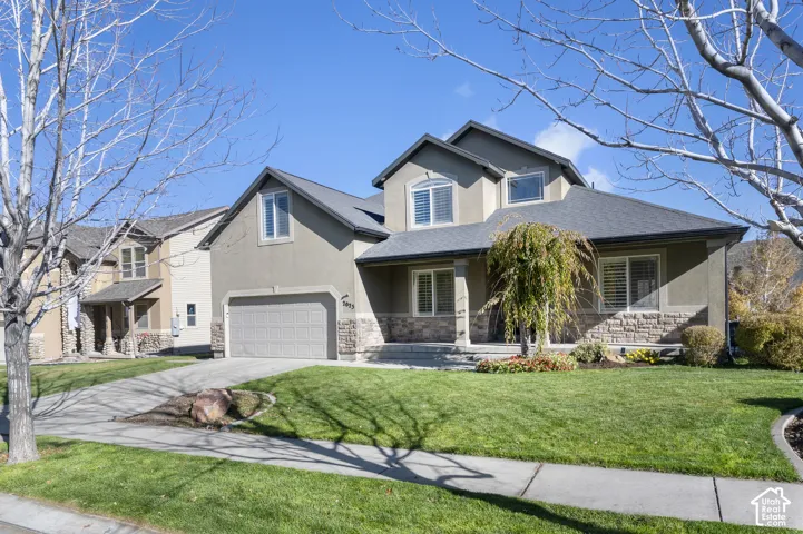 Multi-level exterior featuring stone veneer accents, stucco siding, a multi-gabled roofline, an attached two-car garage, and a covered front entryway