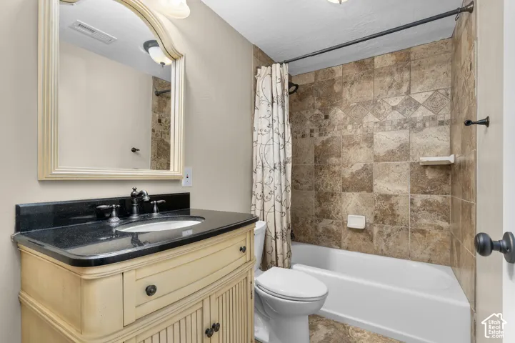 Bathroom vanity with a dark stone countertop, integrated undermount sink, and decorative base cabinetry, complemented by a wall-mounted framed mirror and a tub-shower enclosure featuring textured tile surround with an inlaid accent border