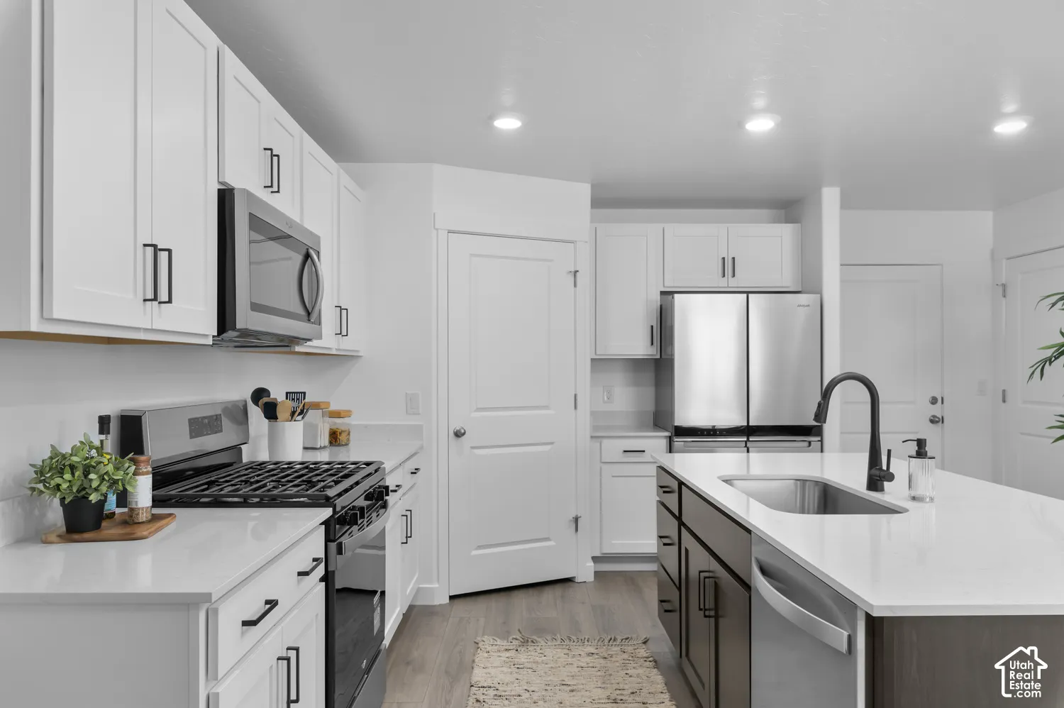 Kitchen featuring white cabinetry, quartz countertops, a central island with a stainless steel sink and matte black faucet, stainless steel appliances, and wood-finish flooring
