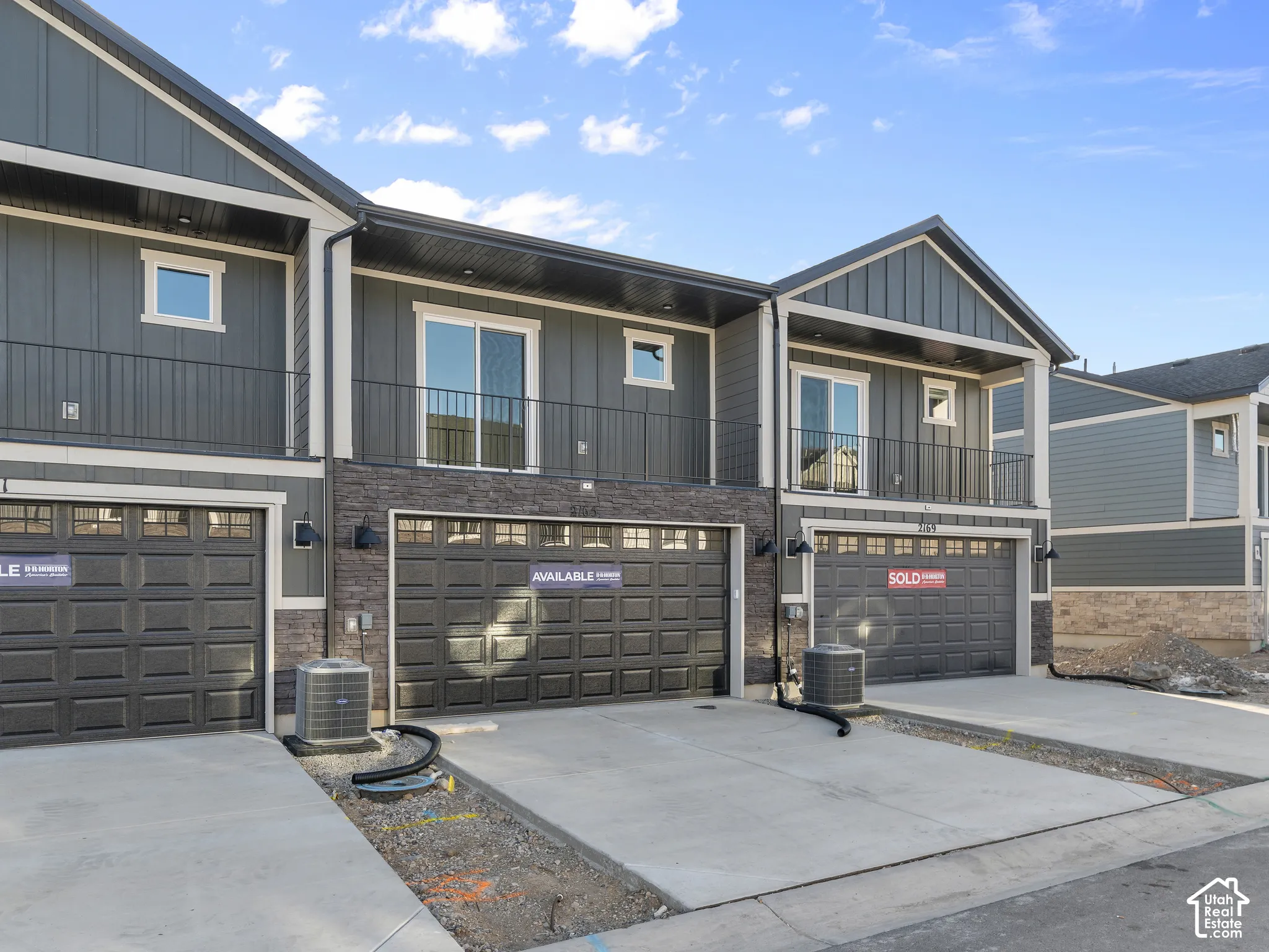 Contemporary exterior featuring vertical siding, stone veneer accents, second-story balconies with iron railings, and multiple attached garage bays