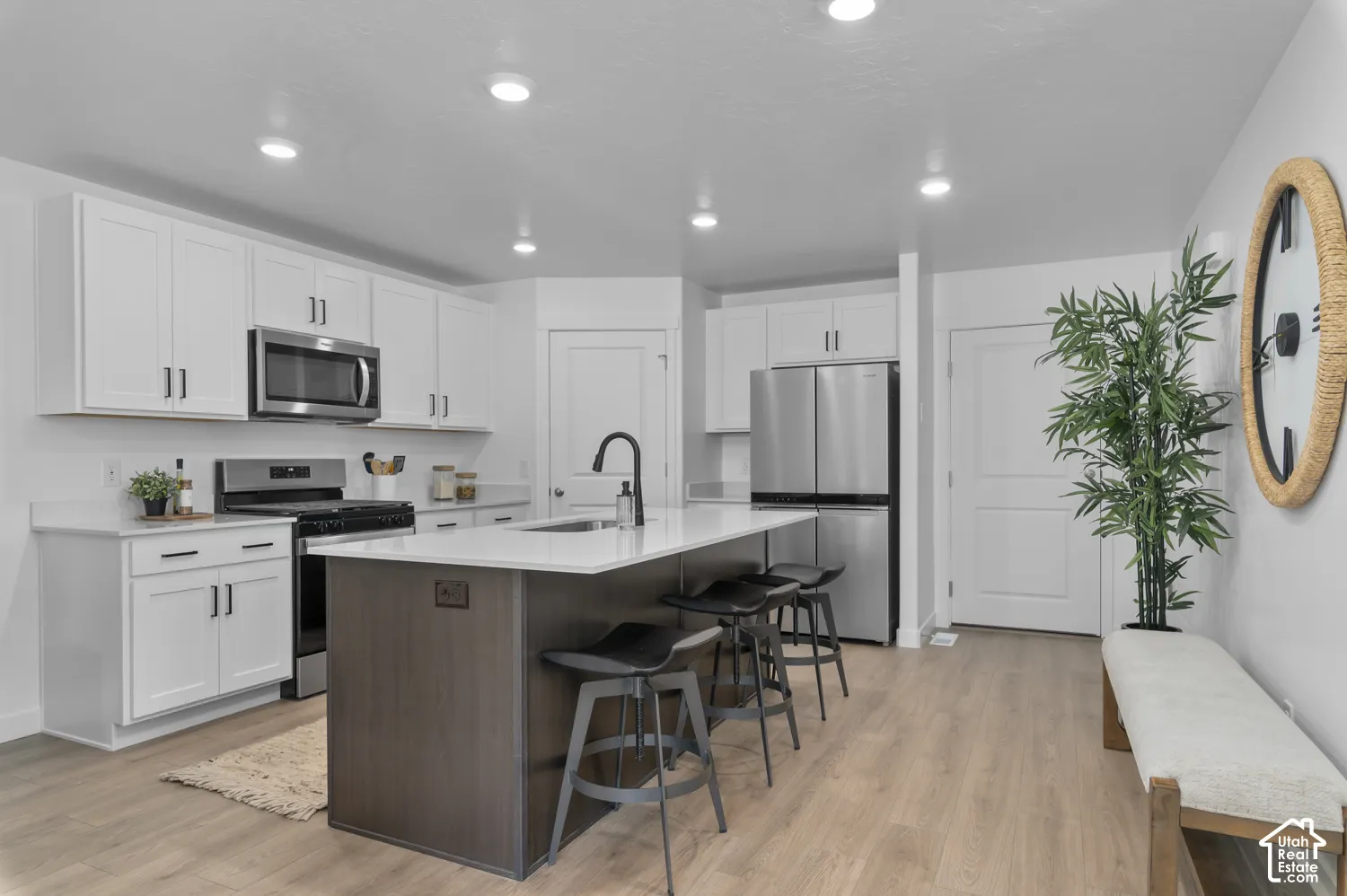 Kitchen featuring white cabinetry, center island with stone-finish countertop, stainless steel appliances, matte black plumbing fixtures, and wood-finish flooring