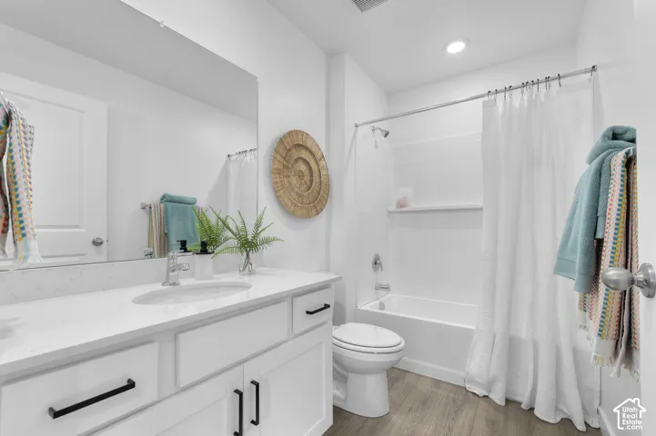 Bathroom featuring a vanity with a white countertop, an integrated oval sink, matte black hardware, a large wall-mounted mirror, and a tub-shower combination with wood-finish flooring