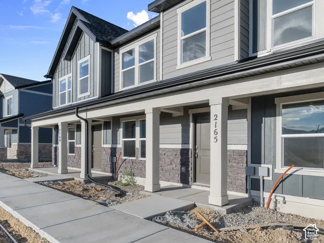 Multi-story exterior featuring fiber cement siding, stone veneer accents, double-hung windows, and a covered front porch with square columns