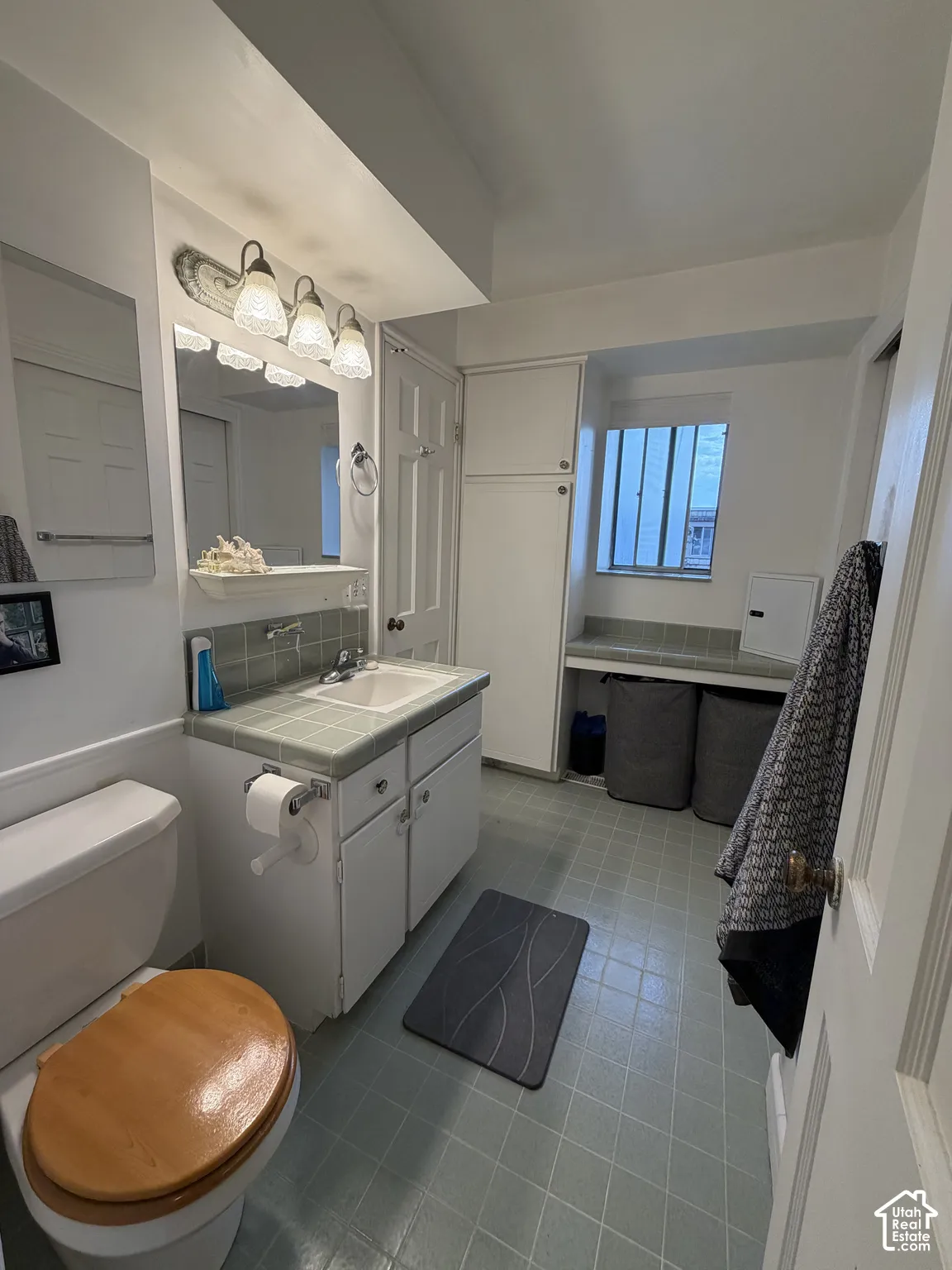 Bathroom featuring a vanity with tile countertop, undermount sink, built-in floor-to-ceiling cabinetry, and tile flooring