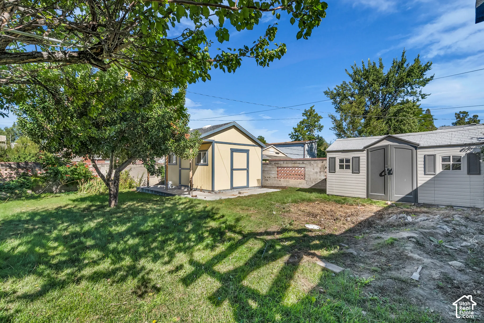 Backyard featuring two storage structures, a concrete patio, mature trees, and a masonry perimeter wall