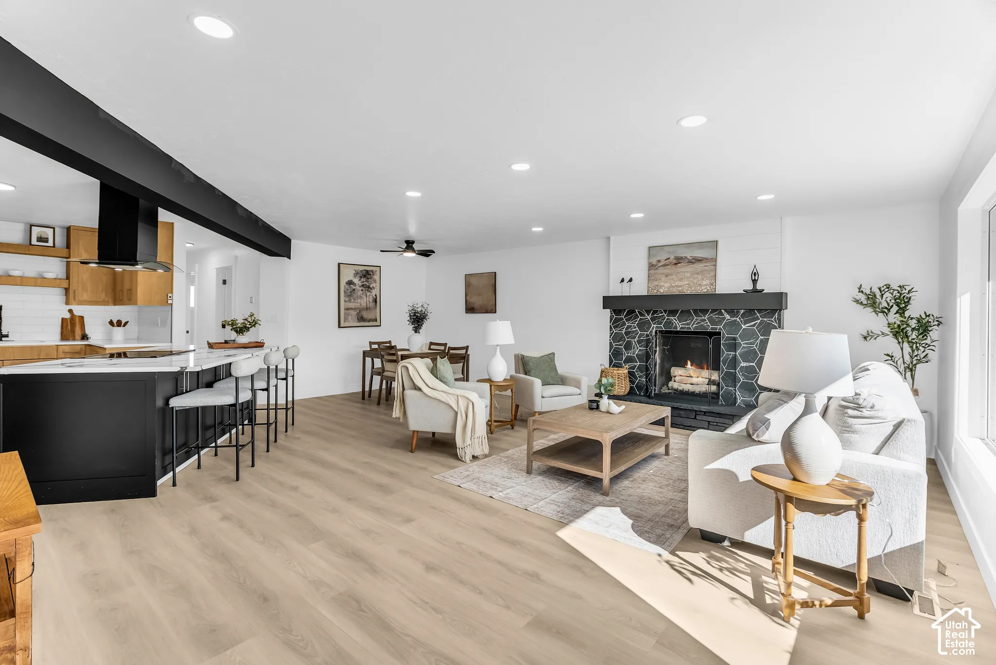 Open-concept interior featuring wood-finish flooring, recessed lighting, a matte black range hood, and a fireplace surround with hexagonal tile