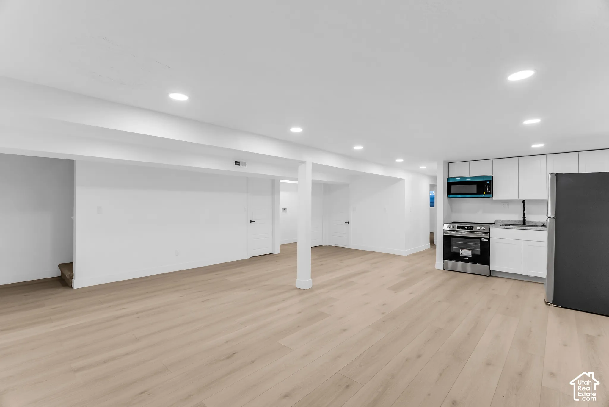 Open-concept space featuring wood-finish flooring, recessed lighting, white cabinetry, and stainless steel appliances
