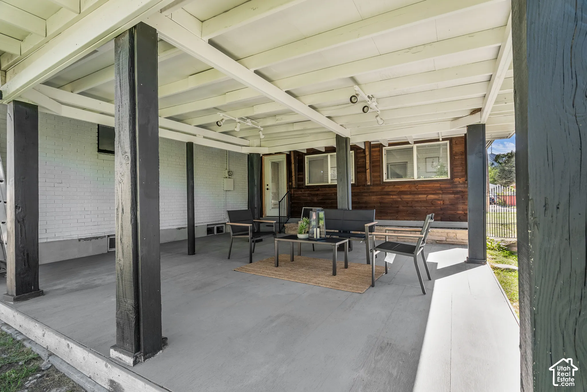 Covered ground-level patio featuring a concrete floor, painted brick walls, natural wood-finish siding, and exposed structural support beams