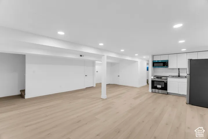 Open-concept space featuring wood-finish flooring, recessed lighting, white cabinetry, and stainless steel appliances
