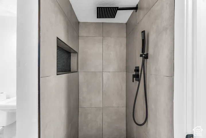 Walk-in shower featuring large-format neutral wall tile, a recessed hexagonal-tile niche, a matte black rainfall showerhead, and a matching handheld sprayer