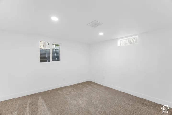 Neutral-toned carpeting, recessed ceiling lighting, and egress window with metal window well