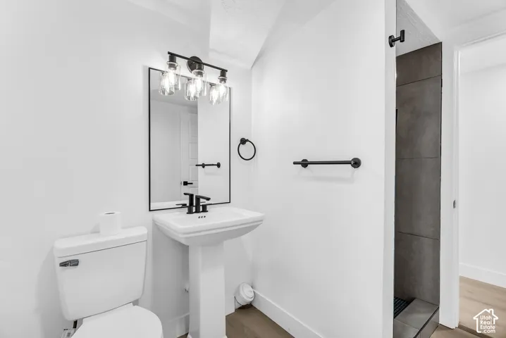 Pedestal sink with a matte black faucet, framed mirror, three-light glass fixture, and dark tile shower surround