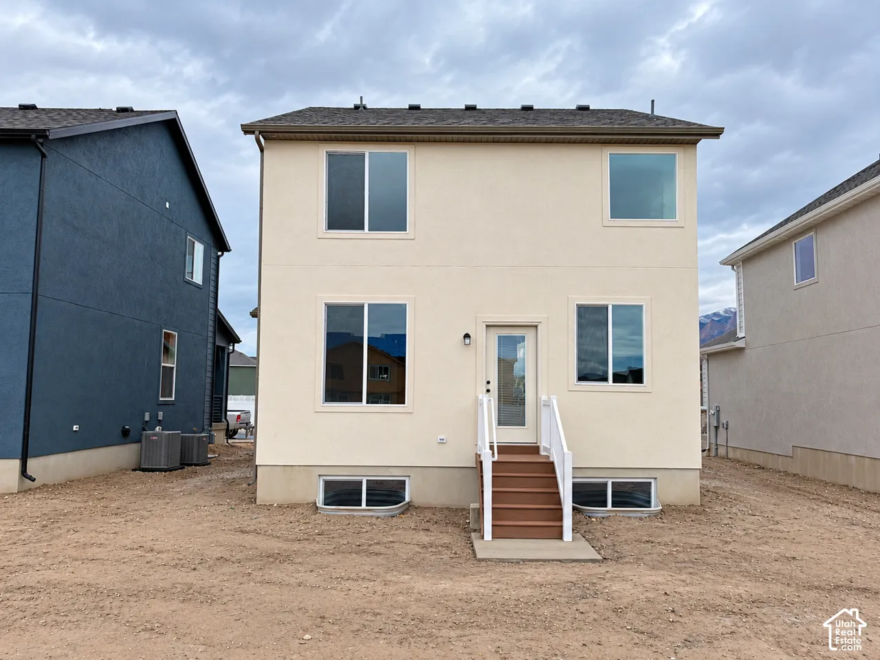 Stucco exterior with wood-finish step entry, white railing, and multiple egress window wells