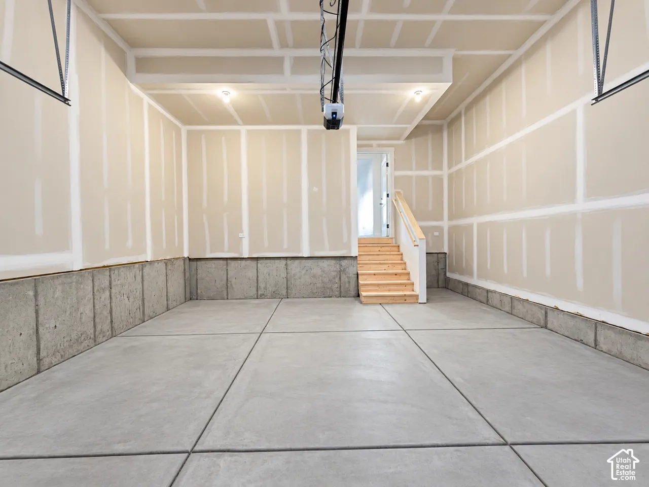 Multi-car garage featuring a concrete floor, finished drywall, concrete foundation walls, and wooden staircase with a wooden handrail
