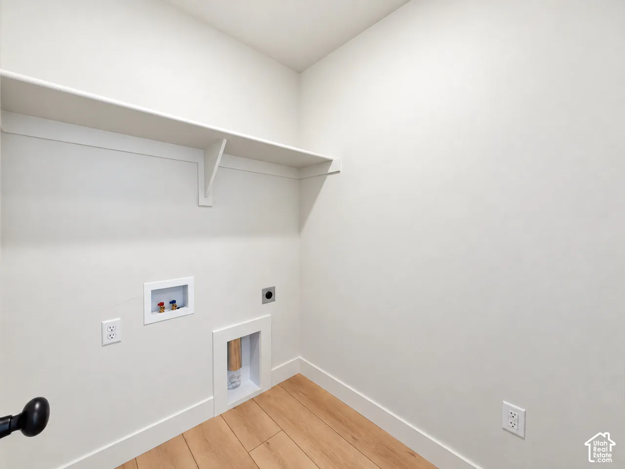 Utility space featuring wood-finish flooring, a wall-mounted shelving unit, and dedicated water and electrical hookups