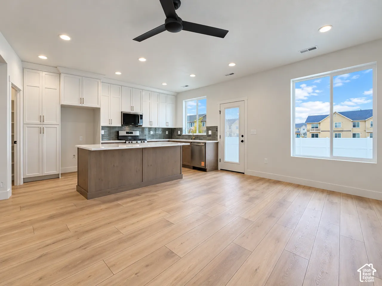 Kitchen featuring wood-finish flooring, white cabinetry, a center island with a solid-surface countertop, recessed ceiling lighting, and a matte black ceiling fan