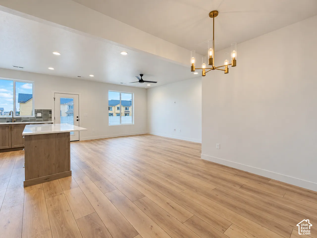 Open-concept interior featuring wood-finish flooring, a kitchen island with stone-finish countertops, recessed lighting, a modern gold-tone multi-light chandelier, and a black ceiling fan