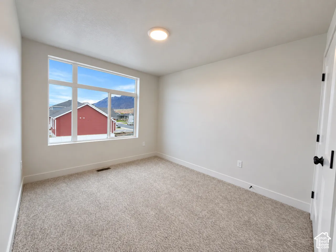 Large window with mountain backdrop, neutral carpeting, and flush-mount ceiling lighting