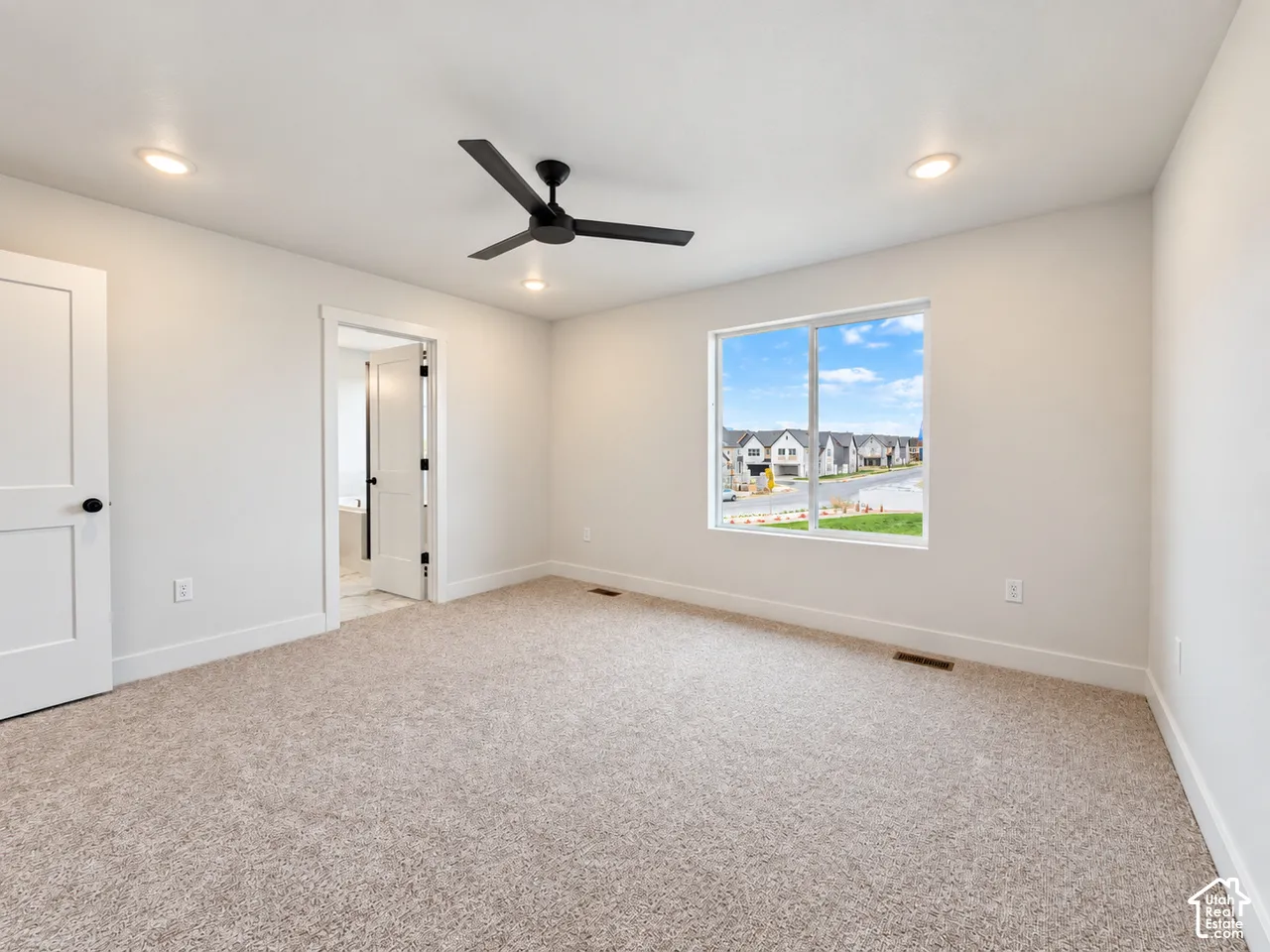 Neutral-toned carpeting, matte black ceiling fan, recessed lighting, and expansive window with exterior window trim