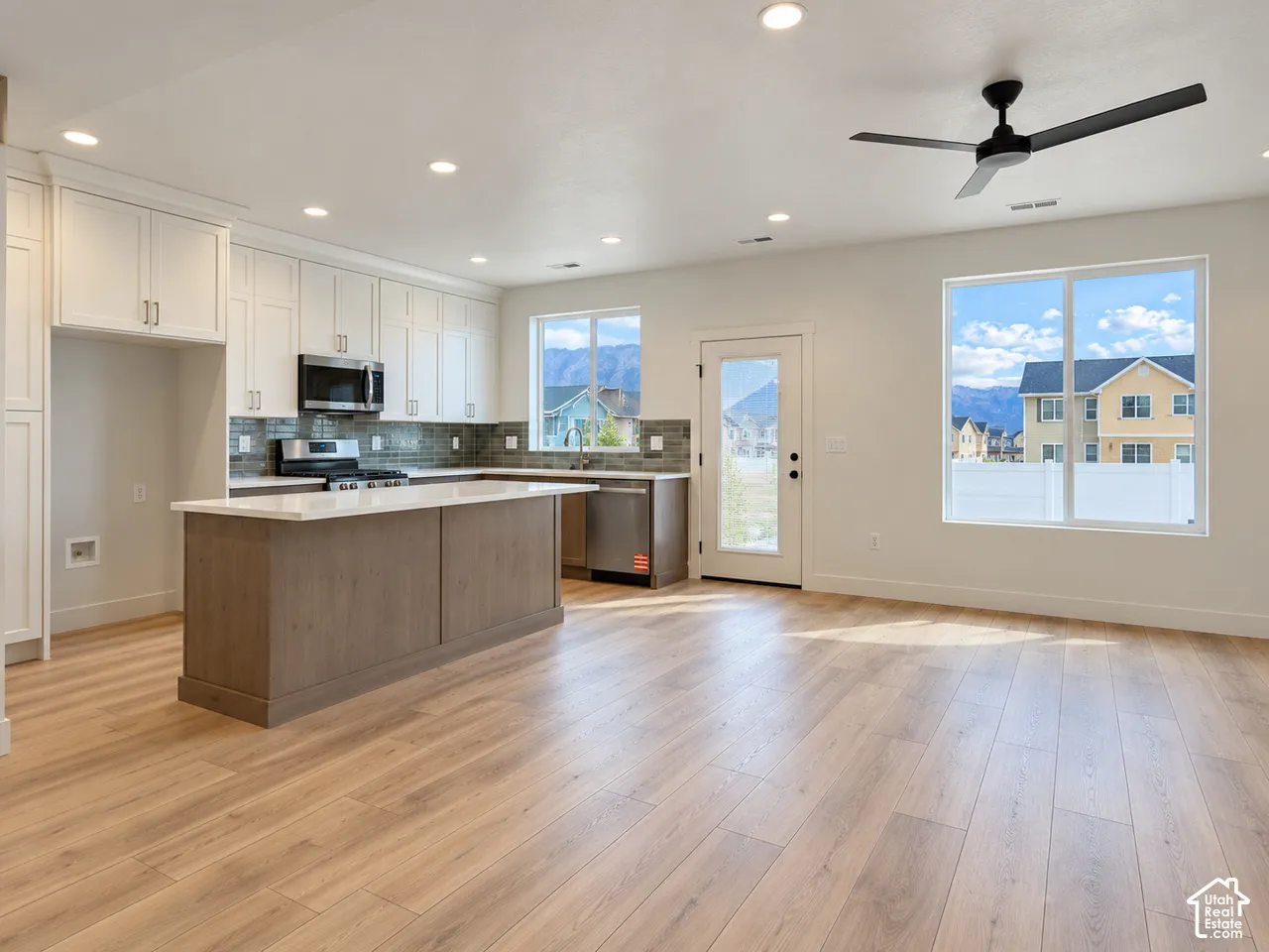 Kitchen featuring a central island with a solid surface countertop, white shaker-style cabinetry, stainless steel appliances, a tiled backsplash, and wood-finish flooring